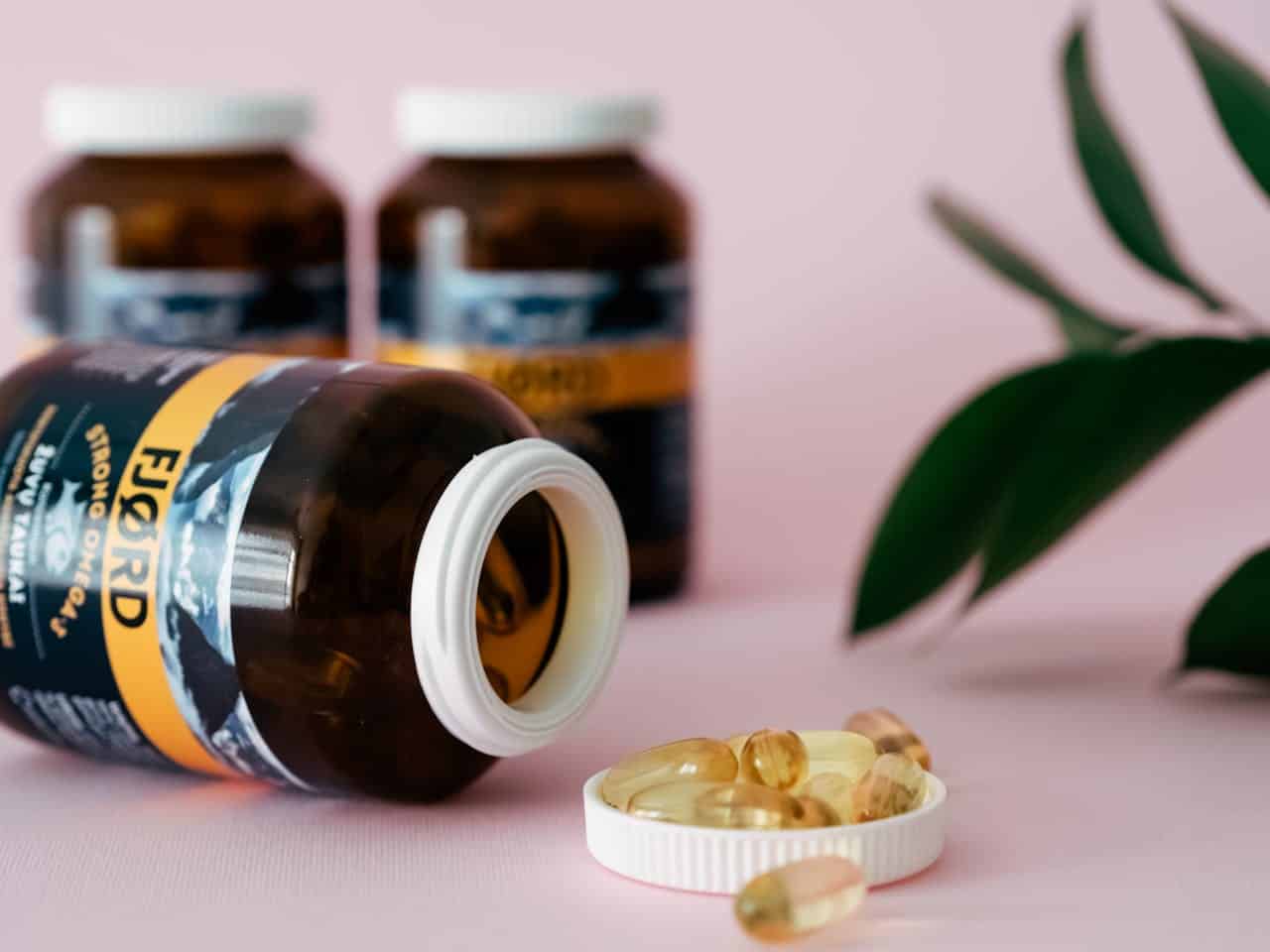 Produtos Close-up of omega-3 capsules and bottles on a pink background, ideal for health and wellness themes.
